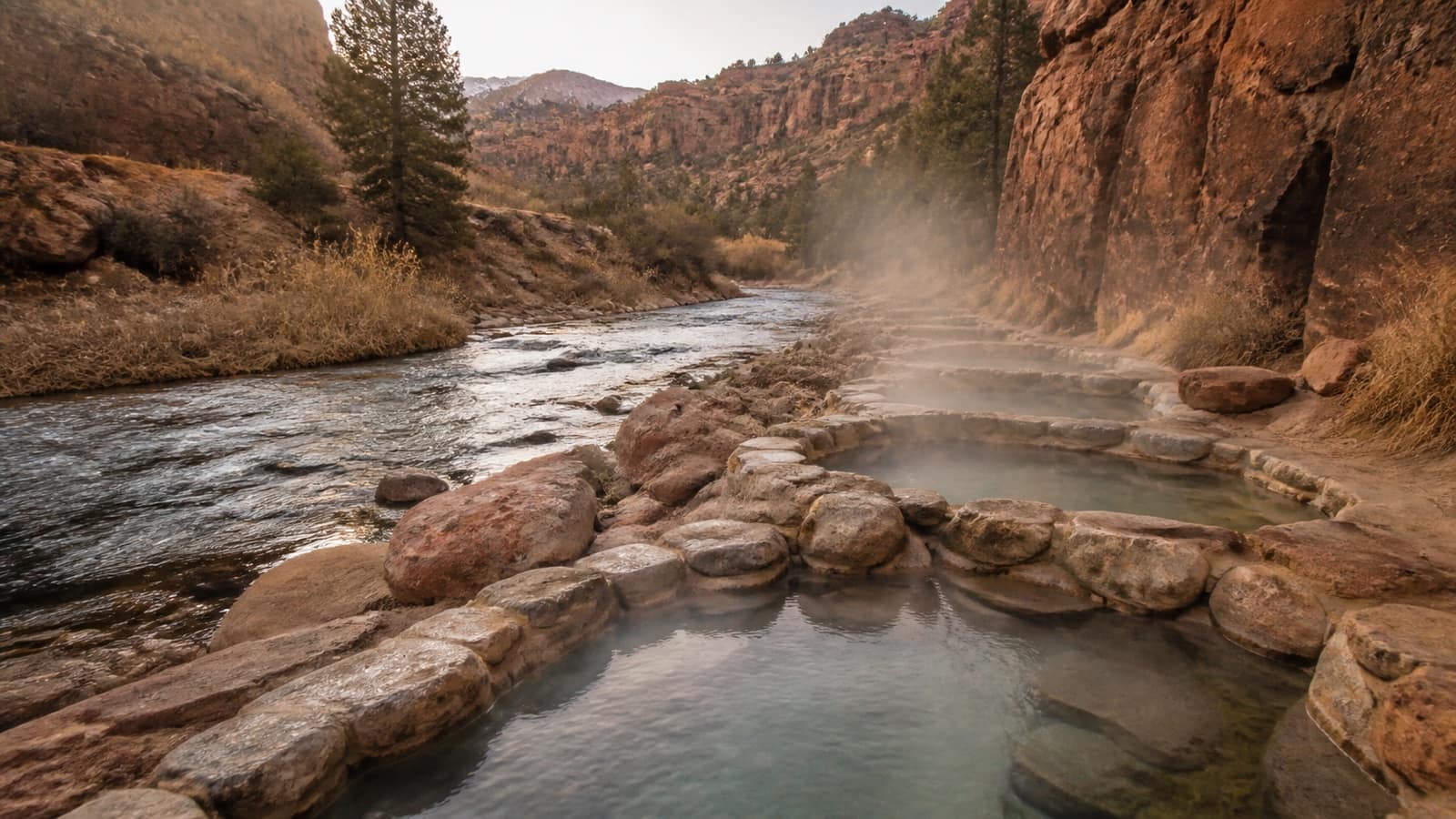Rock-lined hot spring soaking pools along a creek in a Utah canyon