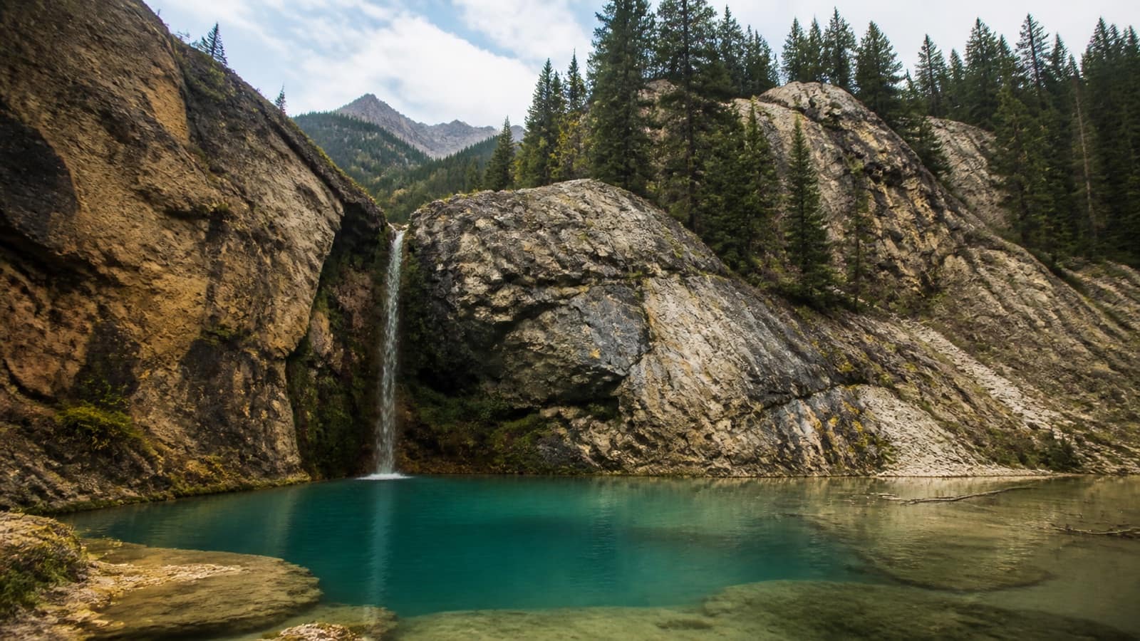 Alpine waterfall feeding a mineral-blue mountain pool ringed by cliffs, Colorado