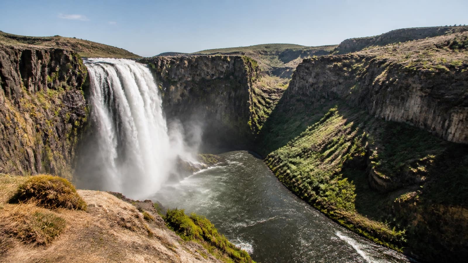 Wide waterfall pouring over a basalt rim into a southern Idaho river canyon