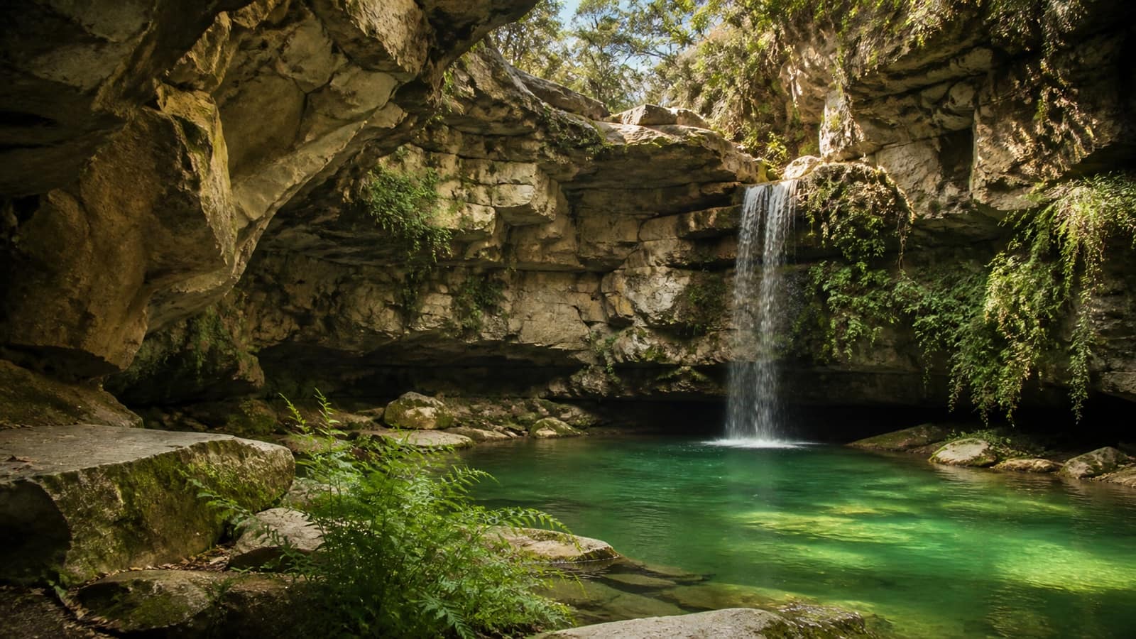 Waterfall feeding a green spring-fed pool inside a Texas Hill Country limestone canyon